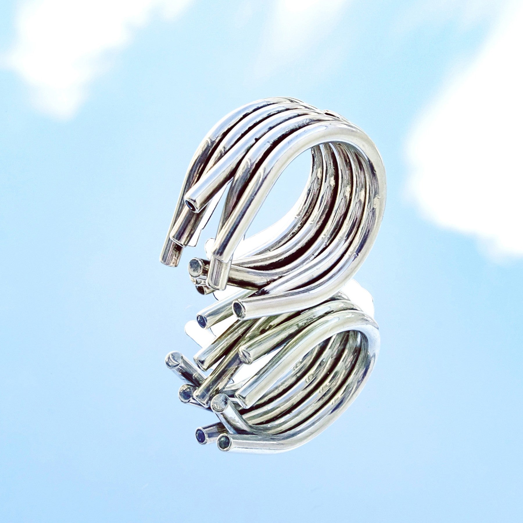 chaotic petite infinity ring in silver with blue sapphires, product image shot on artistic background of a sky reflection, INNAN Jewellery Berlin