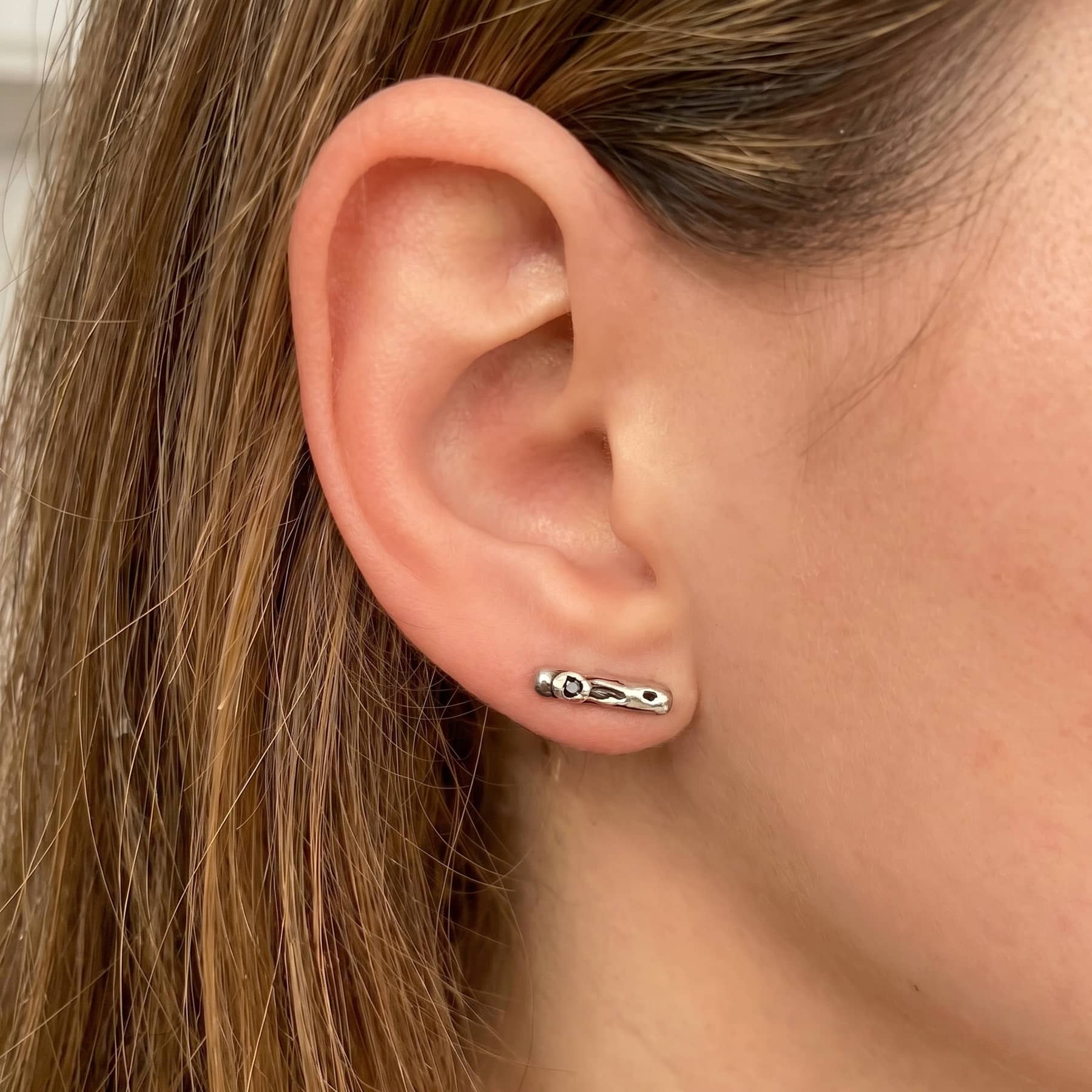 cenote bar earrings in silver with black diamond, worn on ear in close-up, INNAN Jewellery Berlin