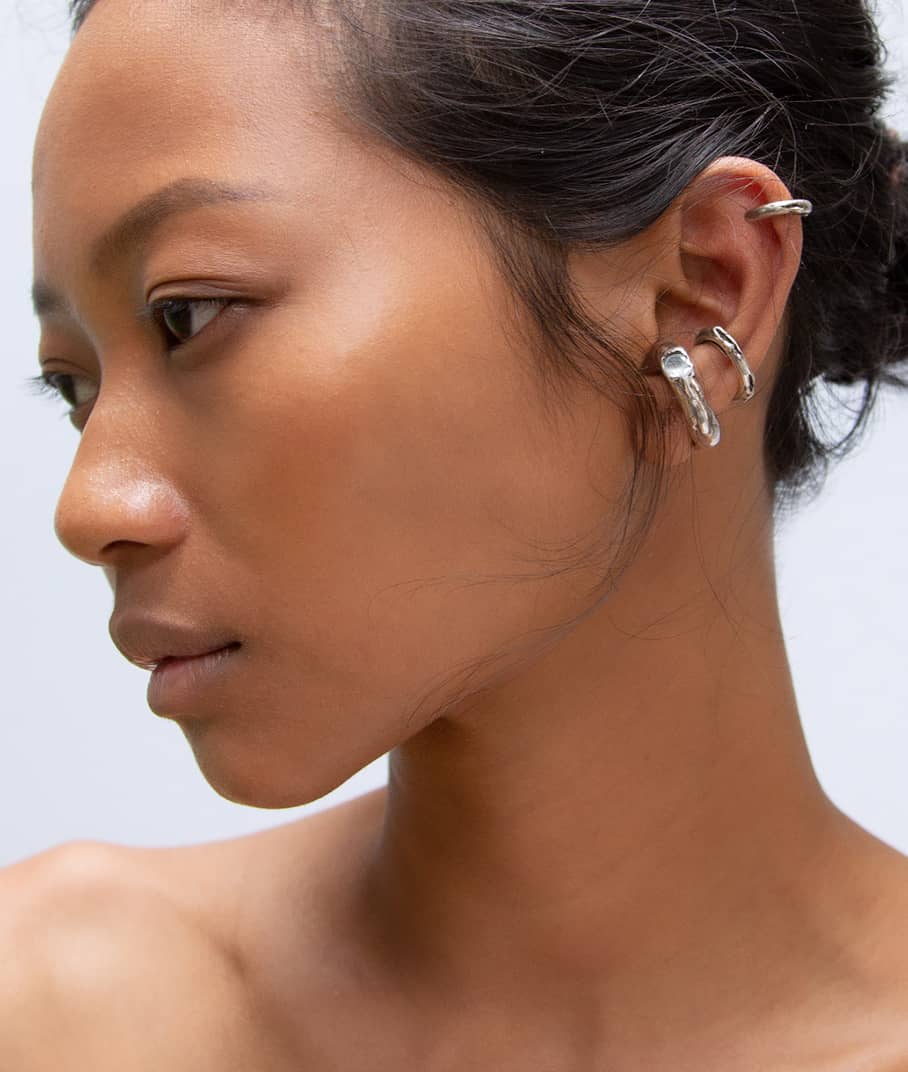 A closeup of a model wearing an Askja Ear cuff with Cenote and Cenote Mini ear cuffs in silver, representing the Cenote collection, INNAN Jewellery Berlin 