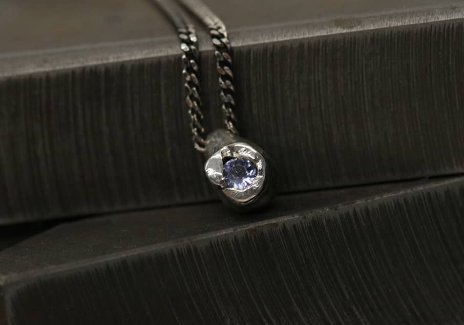 A closeup of a Stilla pendant necklace in silver, with lilac Tanzanite representing the Cenote collection, INNAN Jewellery Berlin 