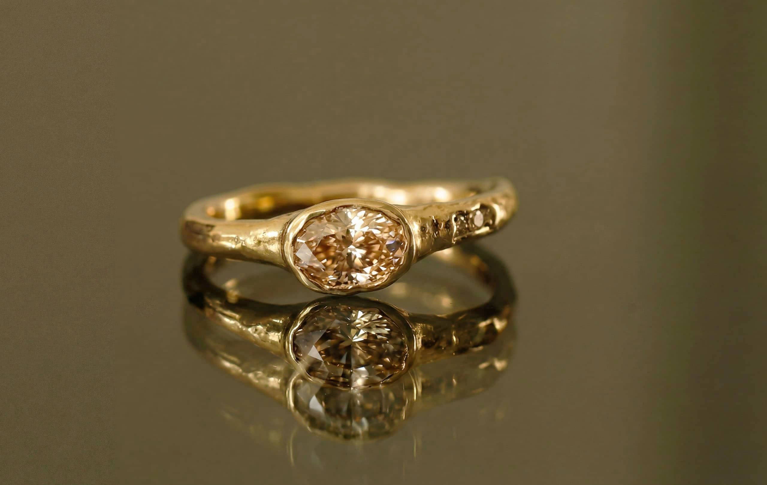 Close-up of bespoke ring in 18 ct yellow gold with a 0.53 ct oval champagne diamond and two matching diamond details by Innan Jewellery